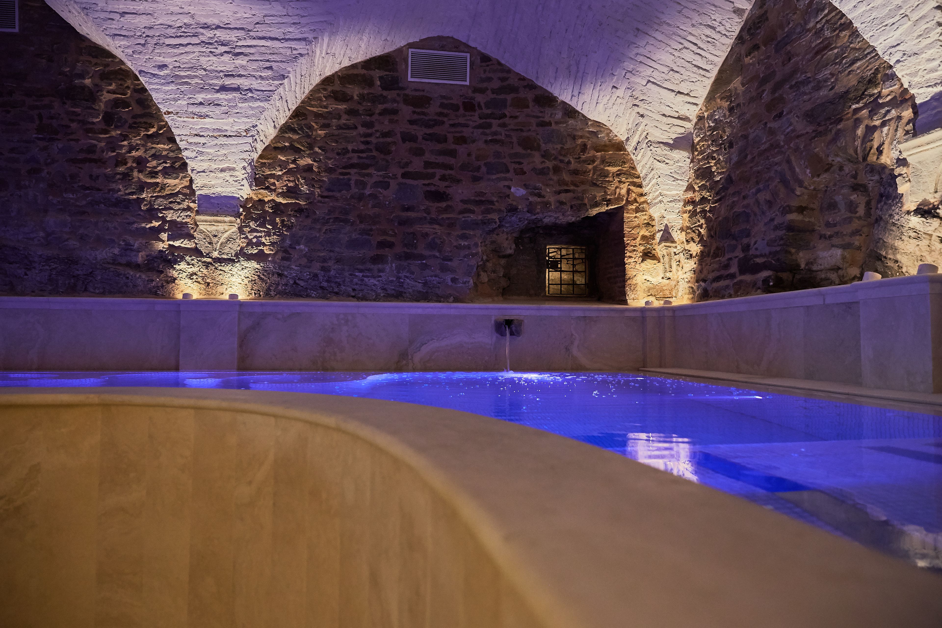 A stone-walled indoor pool with a wooden deck in the foreground.