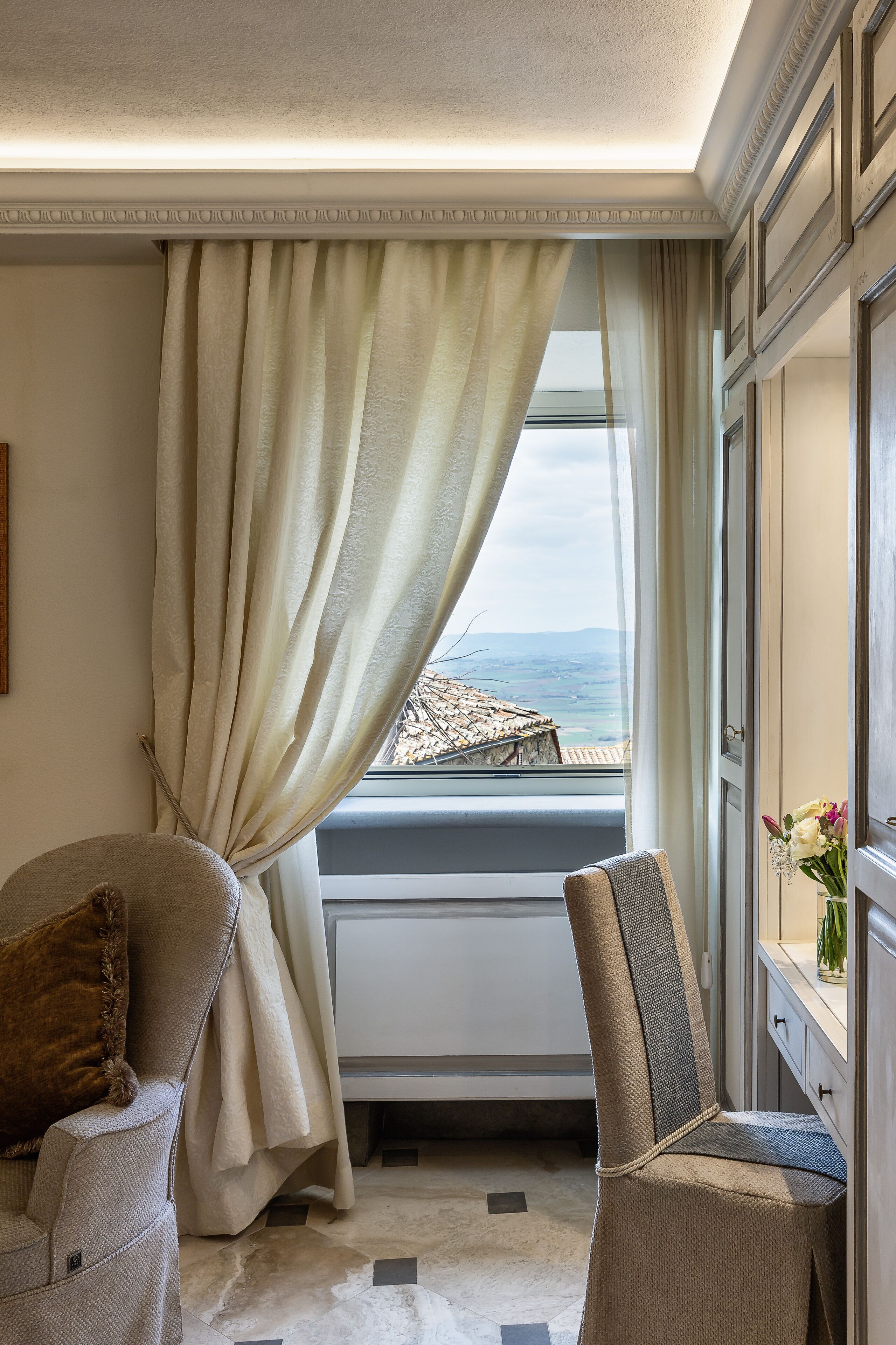 A room with a view of the sea, a window with curtains, a sofa, and a chair.