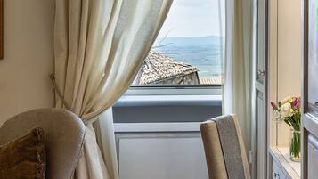 A room with a view of the sea, a window with curtains, a sofa, and a chair.