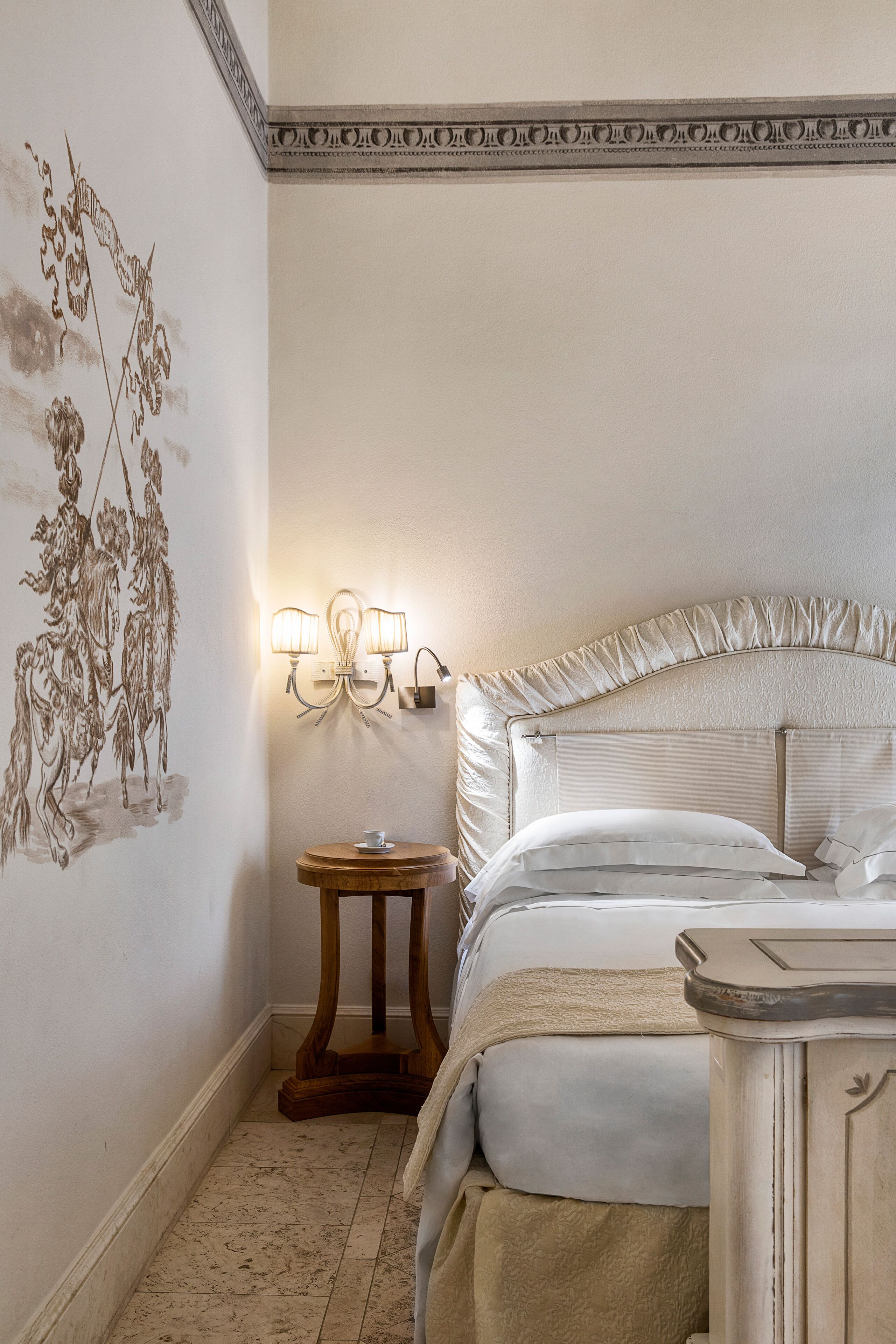 A bedroom with a bed, bedside table, wall art, and a wall-mounted light fixture.