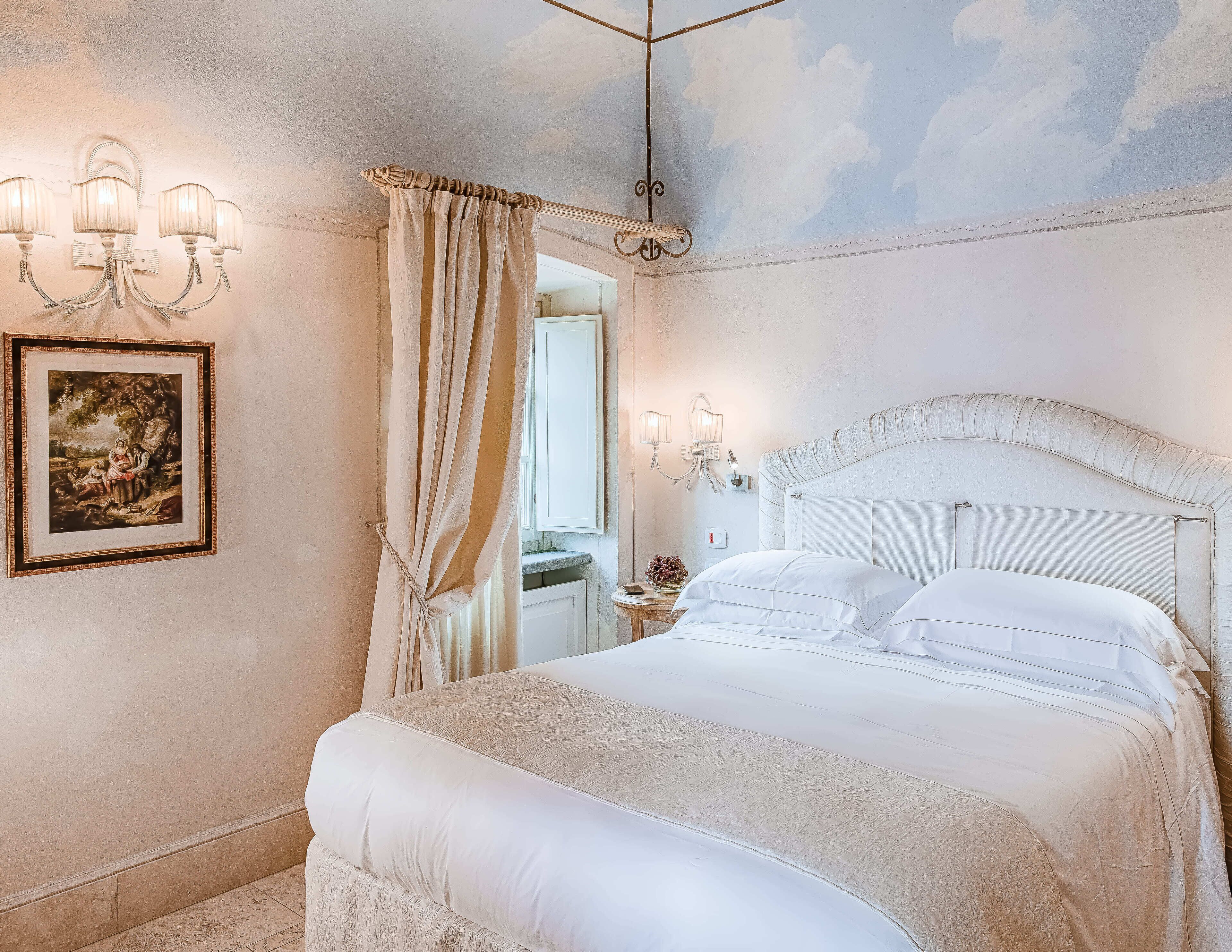 Una camera da letto con un letto grande, un lampadario, un quadro incorniciato e un soffitto decorato con un motivo a nuvole.