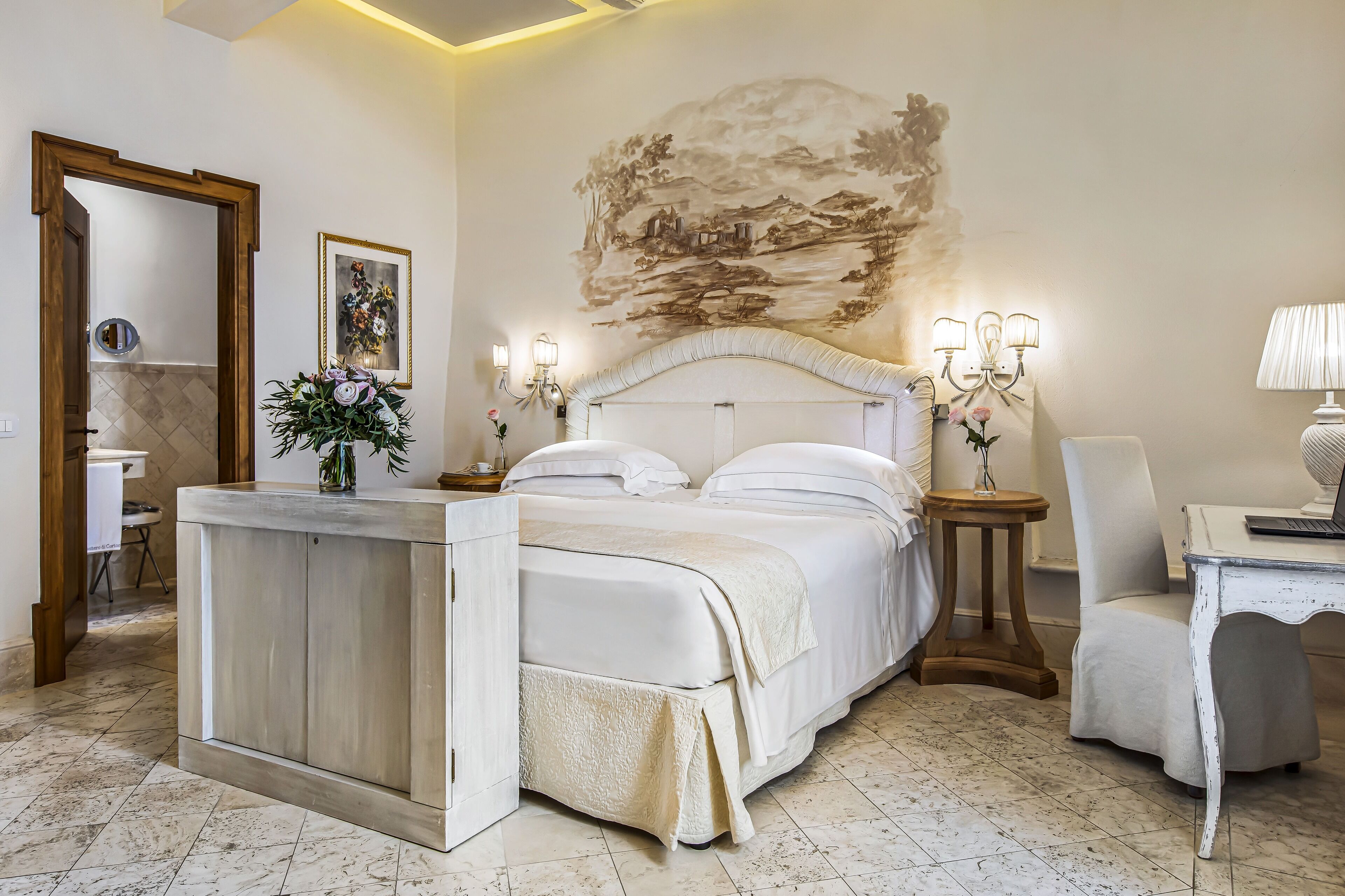 A bedroom with a large bed, a bedside table, a chair, a desk, and a wall mural.