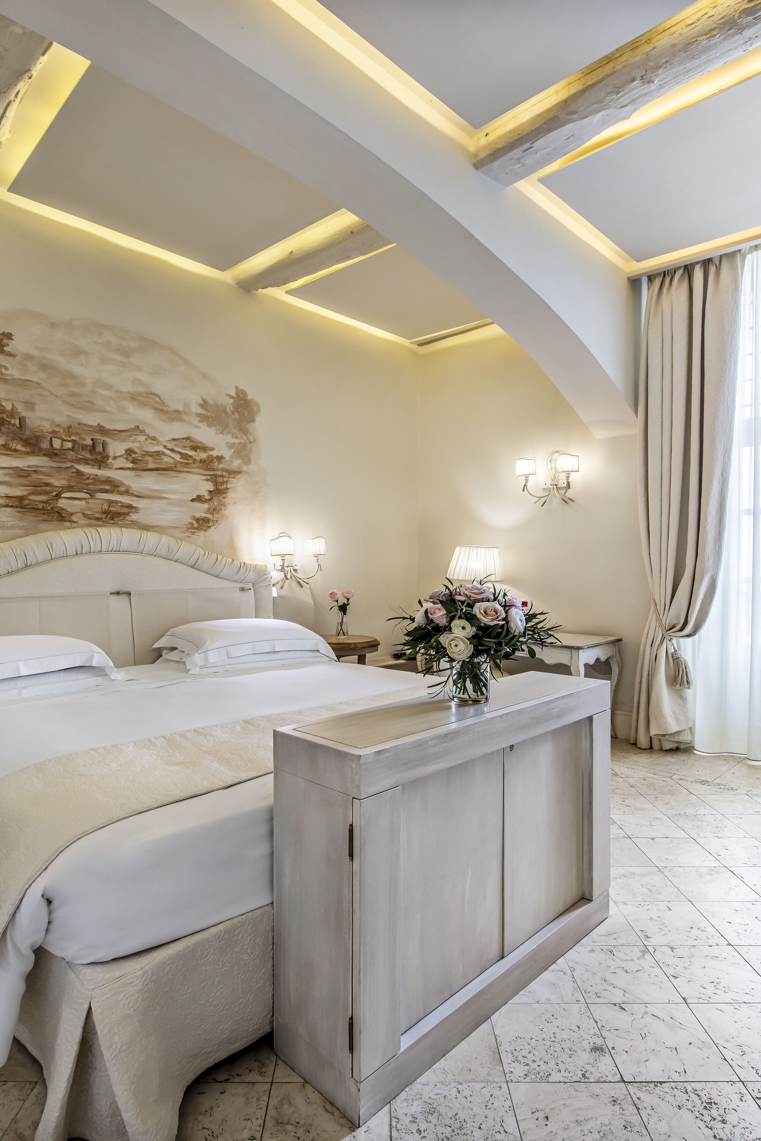 Habitación de hotel con cama, mesitas de noche, un florero decorativo y un cuadro en la pared.