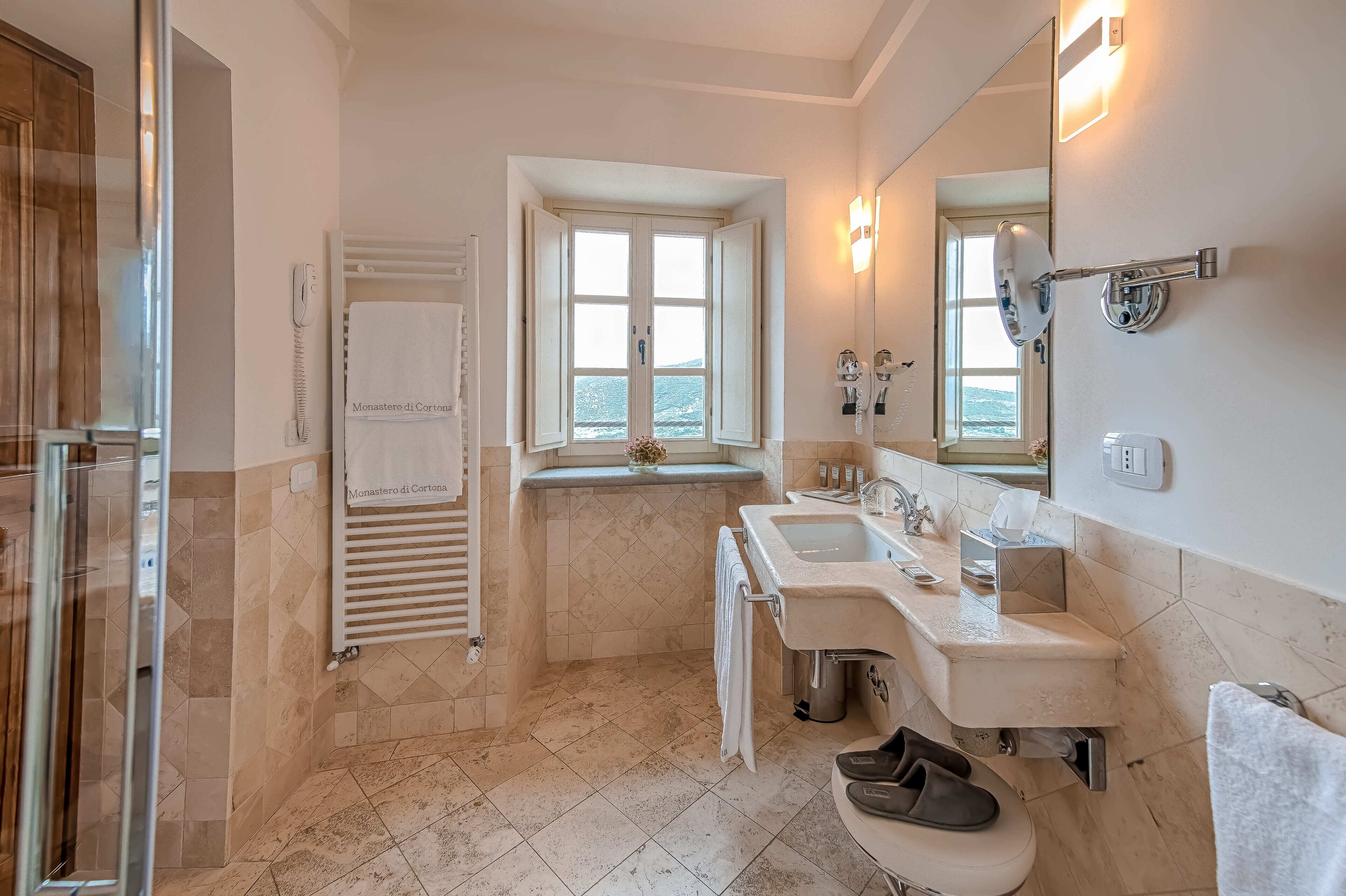 Een badkamer met een douche, twee wasbakken, een spiegel en een raam met uitzicht.