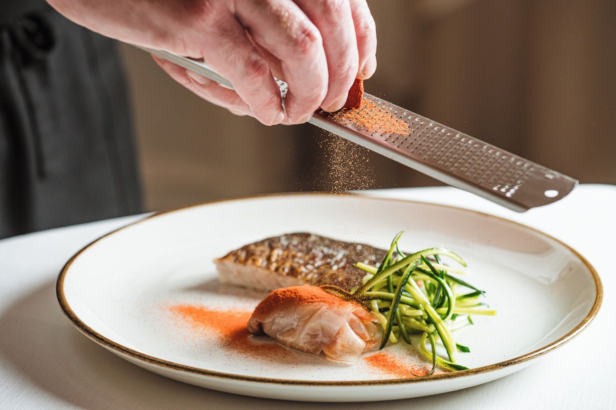 A person grating a spice over a dish with fish and vegetables.