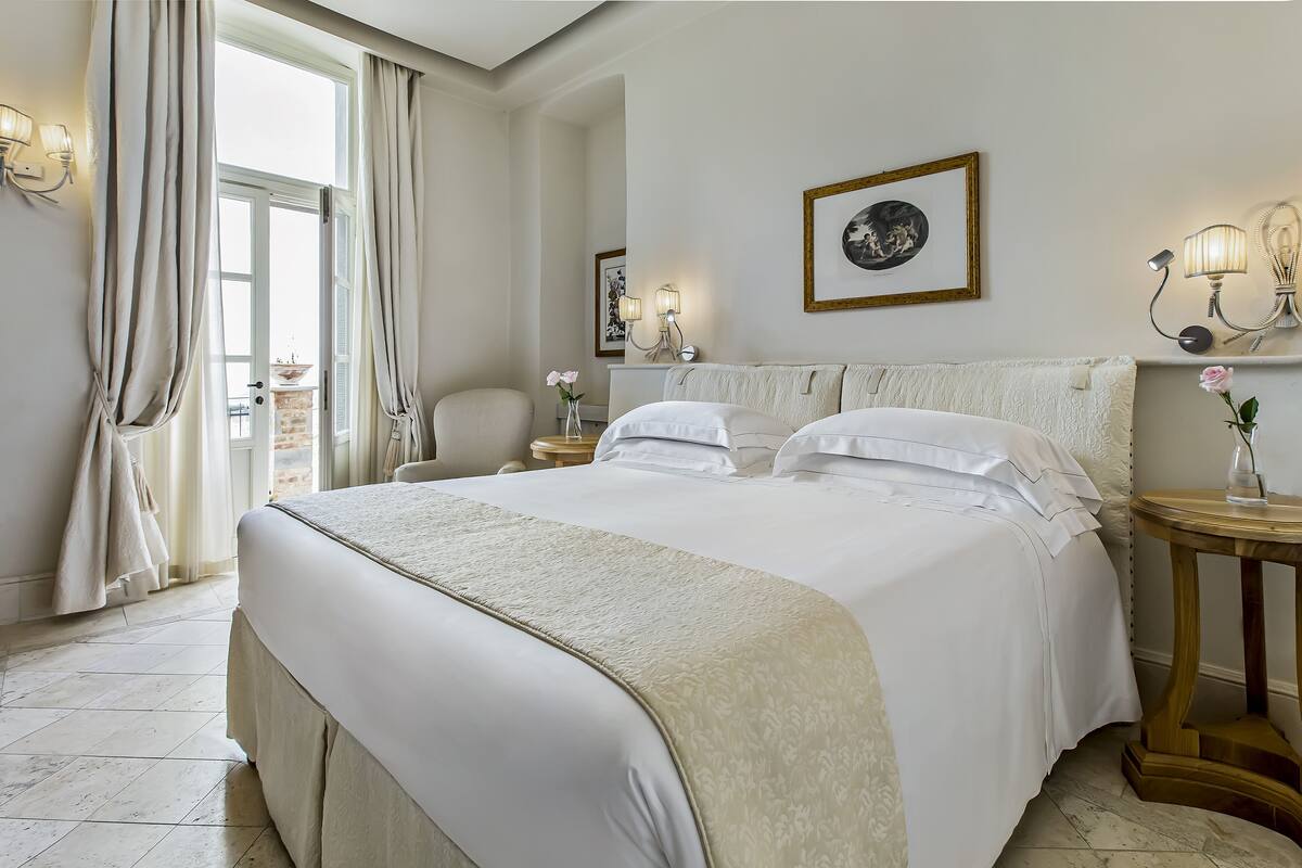 Een ruime slaapkamer met een groot bed, een nachtkastje met lamp en uitzicht op het omliggende landschap door een raam.