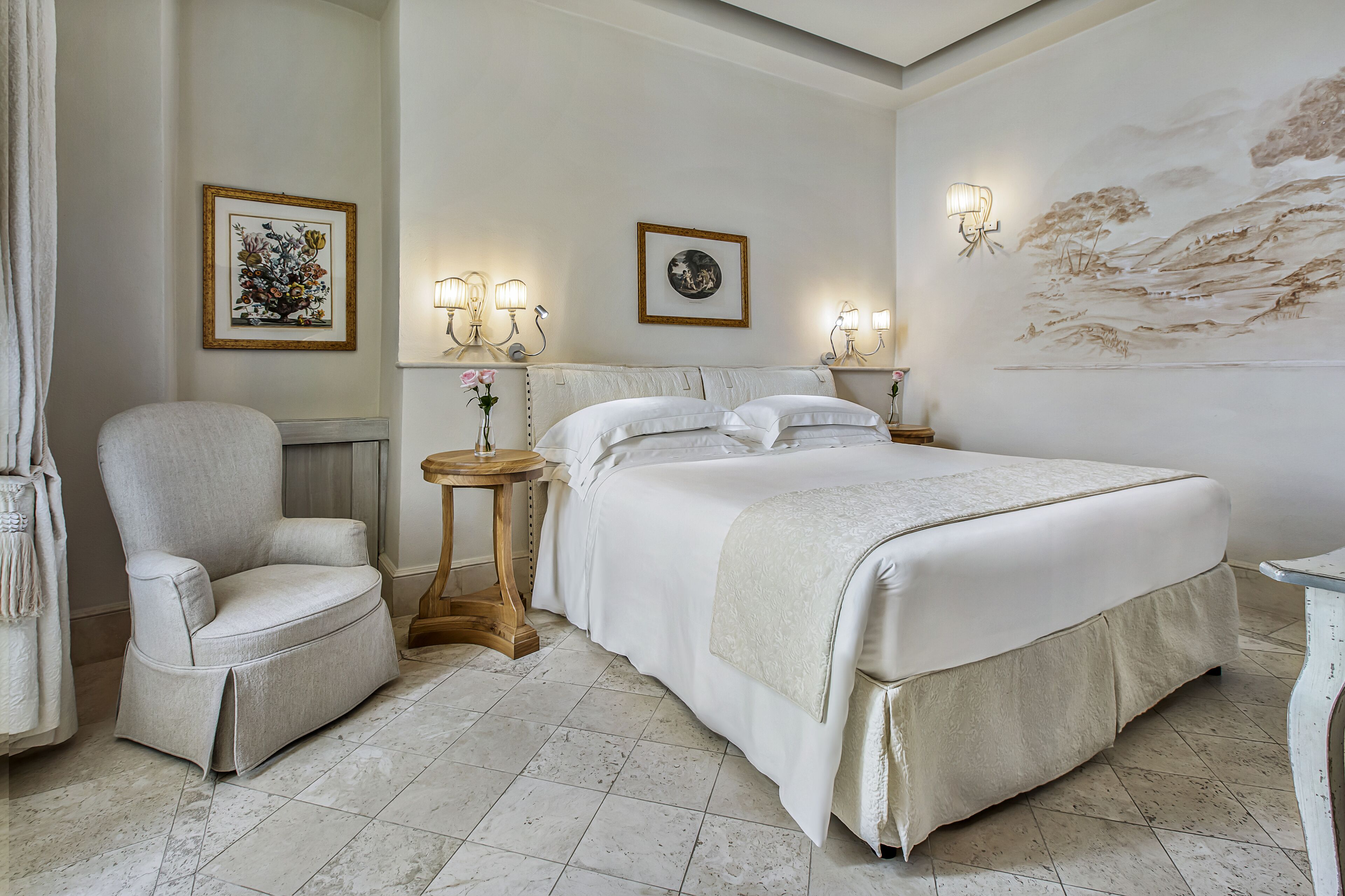 A hotel room with a large bed, a chair, a small table with a vase, and wall-mounted lamps.