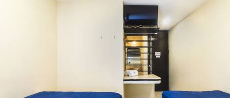 A small hotel room with two single beds, a kitchenette, and a bathroom.