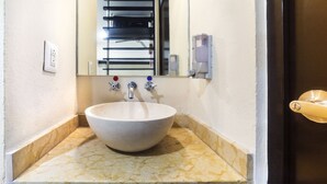 A bathroom with a large, round vessel sink, a mirror, a towel rack, and a soap dispenser. - Hotel Kapu Puebla (Puebla)