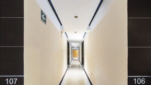 A hotel hallway with numbers 106 and 107 on the walls, a directional sign, and a bright exit at the end. - Hotel Kapu Puebla (Puebla)