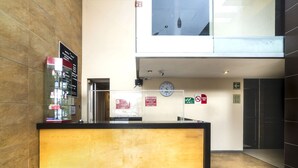 A reception desk with a clock, emergency exit signs, and a directory on the wall. - Hotel Kapu Puebla (Puebla)
