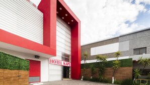 A modern hotel with a prominent red and white facade, a visible entrance, and a well-maintained garden area. - Hotel Kapu Puebla (Puebla)