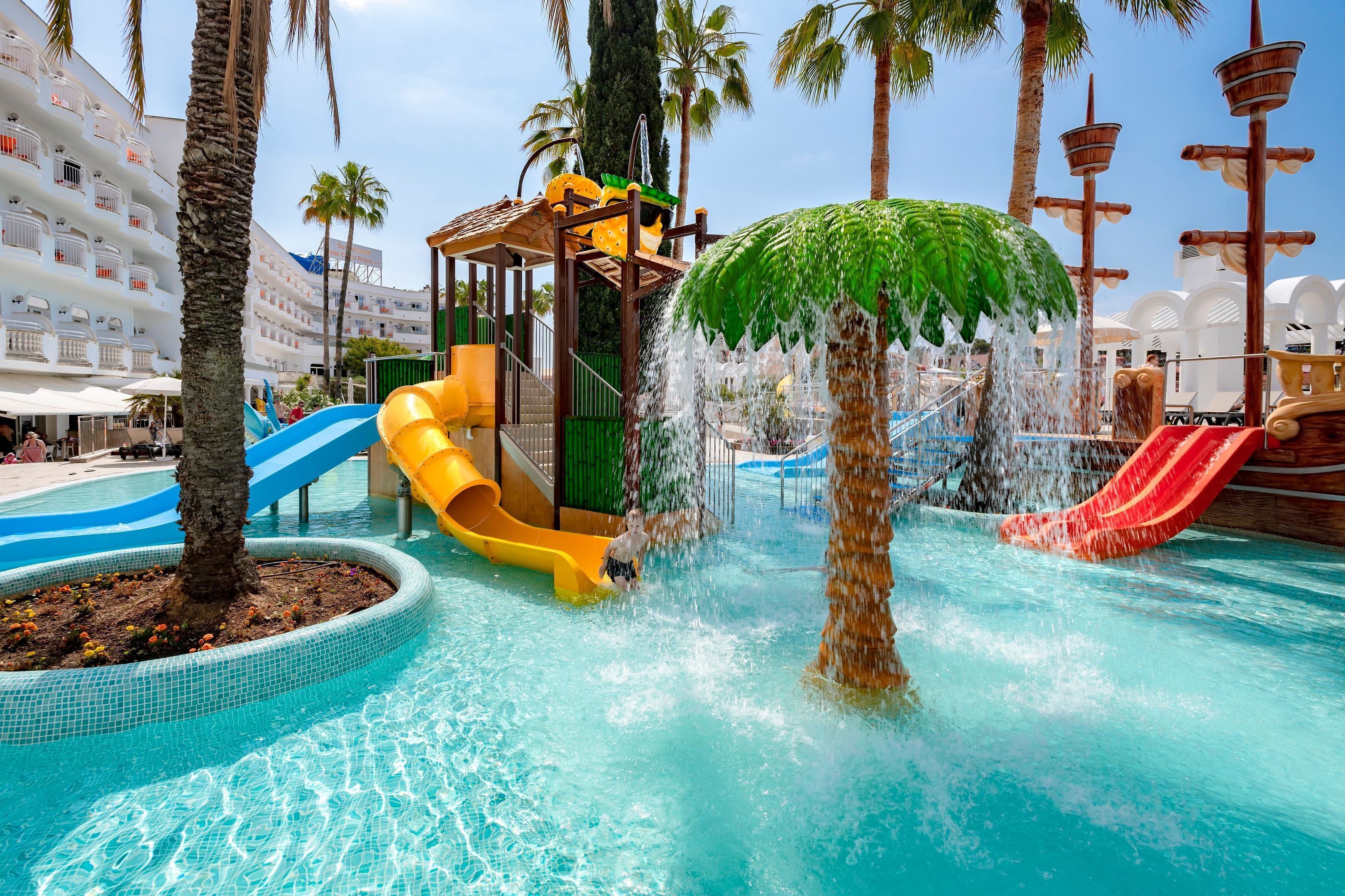 Ein Wasserpark mit Rutschen und Wasserspielen, umgeben von Palmen und einem Schwimmbecken.