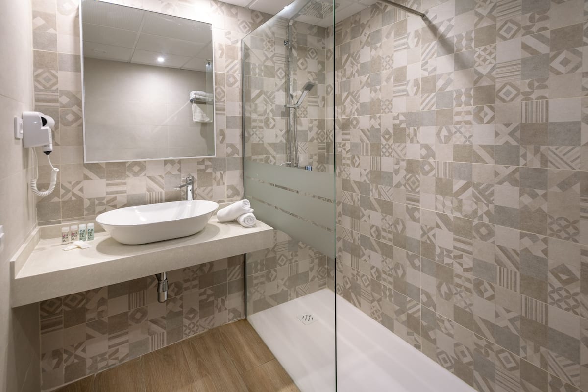 Une salle de bain moderne avec un grand miroir, un lavabo et un espace douche.