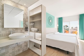 Habitación de hotel moderna con un espejo grande, un lavamanos blanco, un secador de pelo, una cama con sábanas blancas y vistas al exterior a través de una ventana con cortinas azul verdoso.