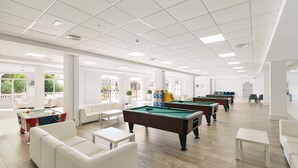 Un área recreativa amplia y techada con varias mesas de billar, asientos cómodos y grandes ventanales que brindan luz natural.