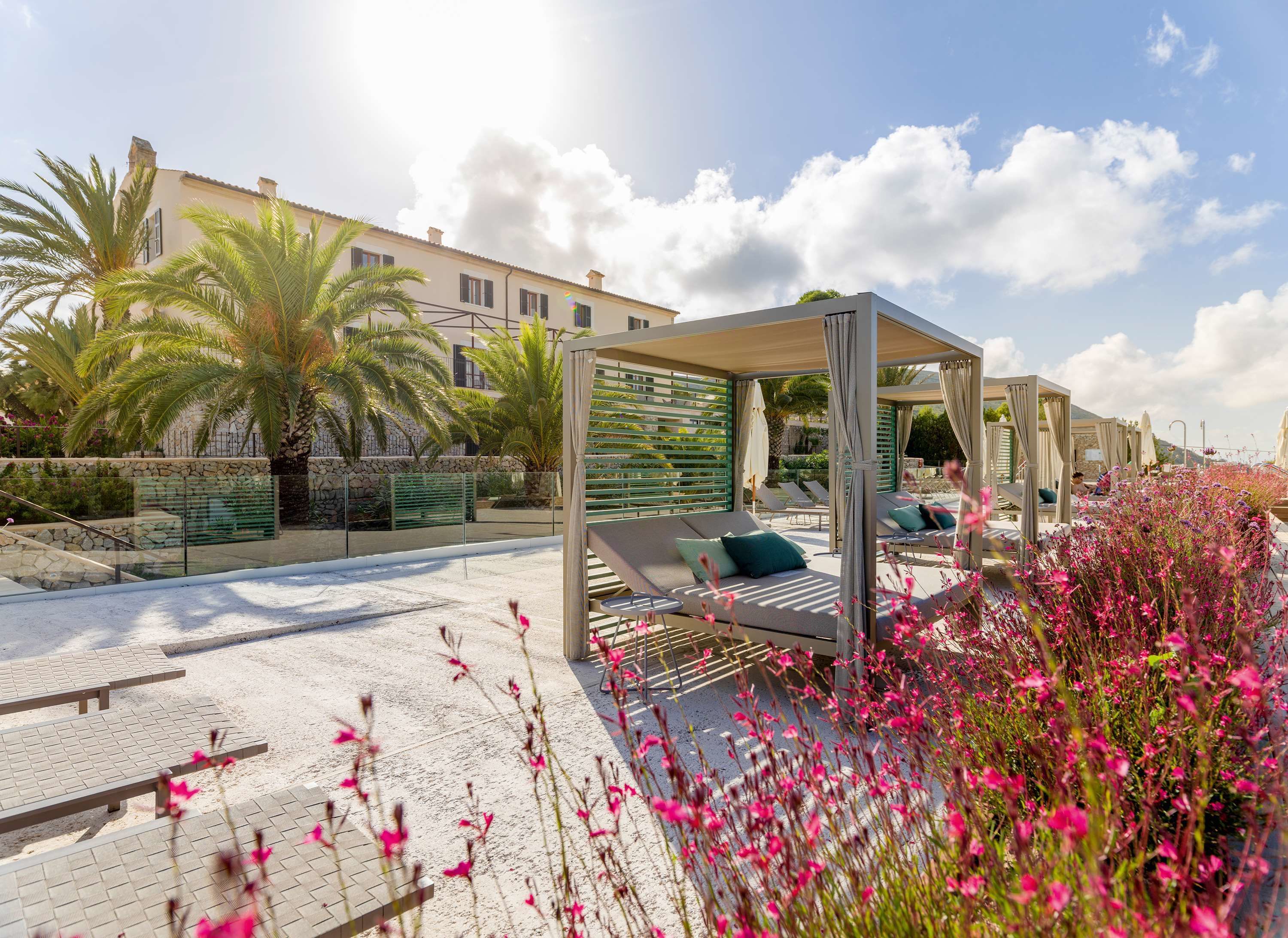 A poolside area with sun loungers, a covered seating area, and a stone wall with greenery.