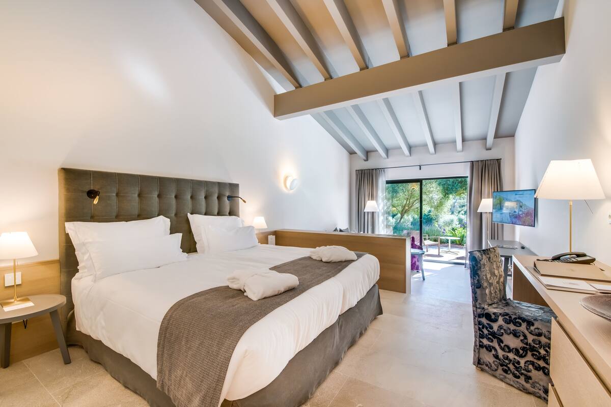 A modern hotel room with a large bed, a desk, and a view of the outdoors.