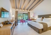 A hotel room with a large bed, a desk with a chair, a small table, and a balcony with chairs.