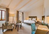 A hotel room with a bed, two armchairs, a small table, a desk, and a lamp.