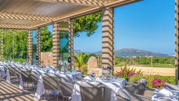 Un espacio de comedor al aire libre con mesas preparadas para dos, con vistas a un paisaje pintoresco con montañas y un viñedo.