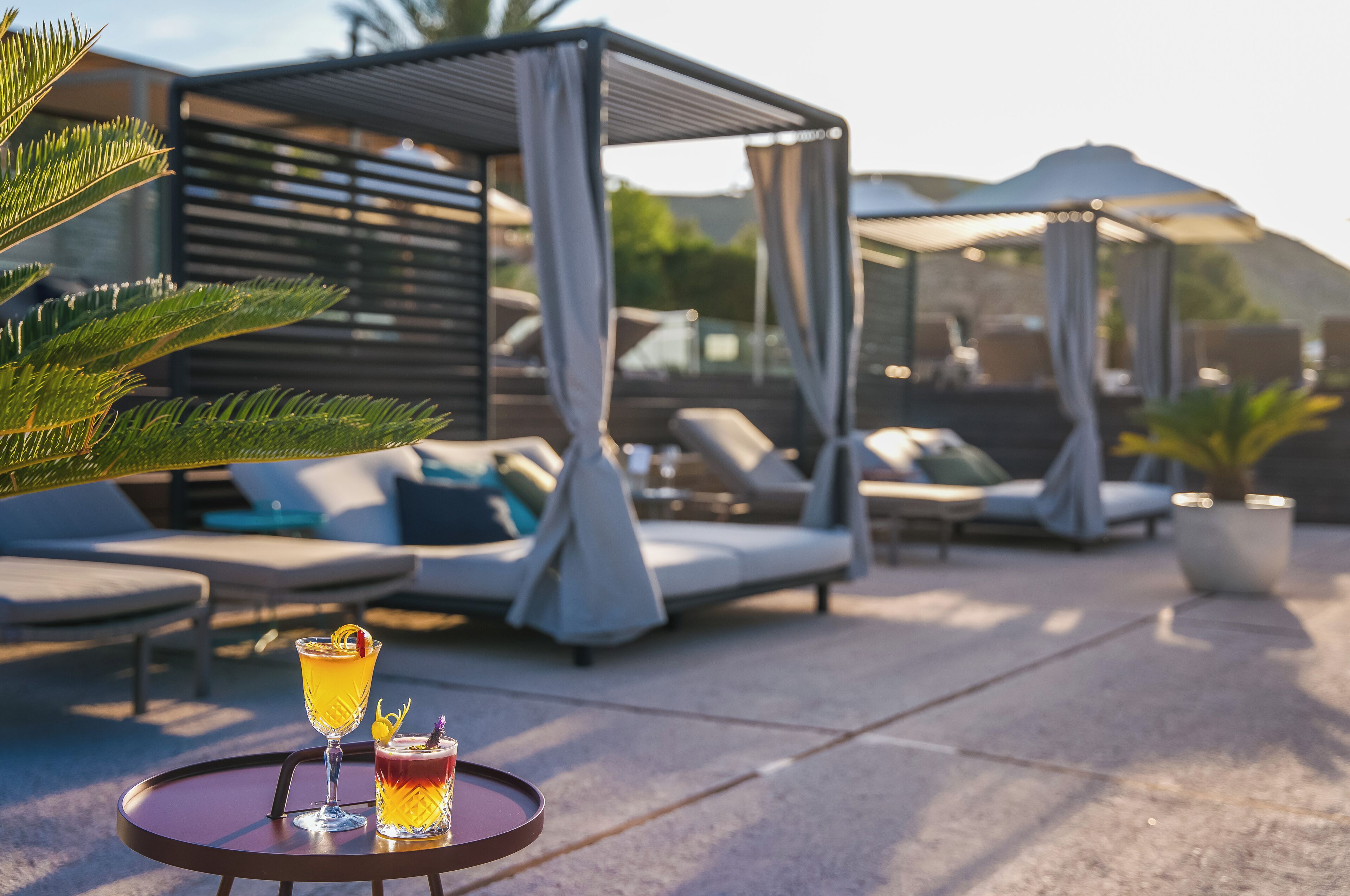 Un área de descanso al aire libre con sillones reclinables, una zona de estar cubierta y una mesa con bebidas.