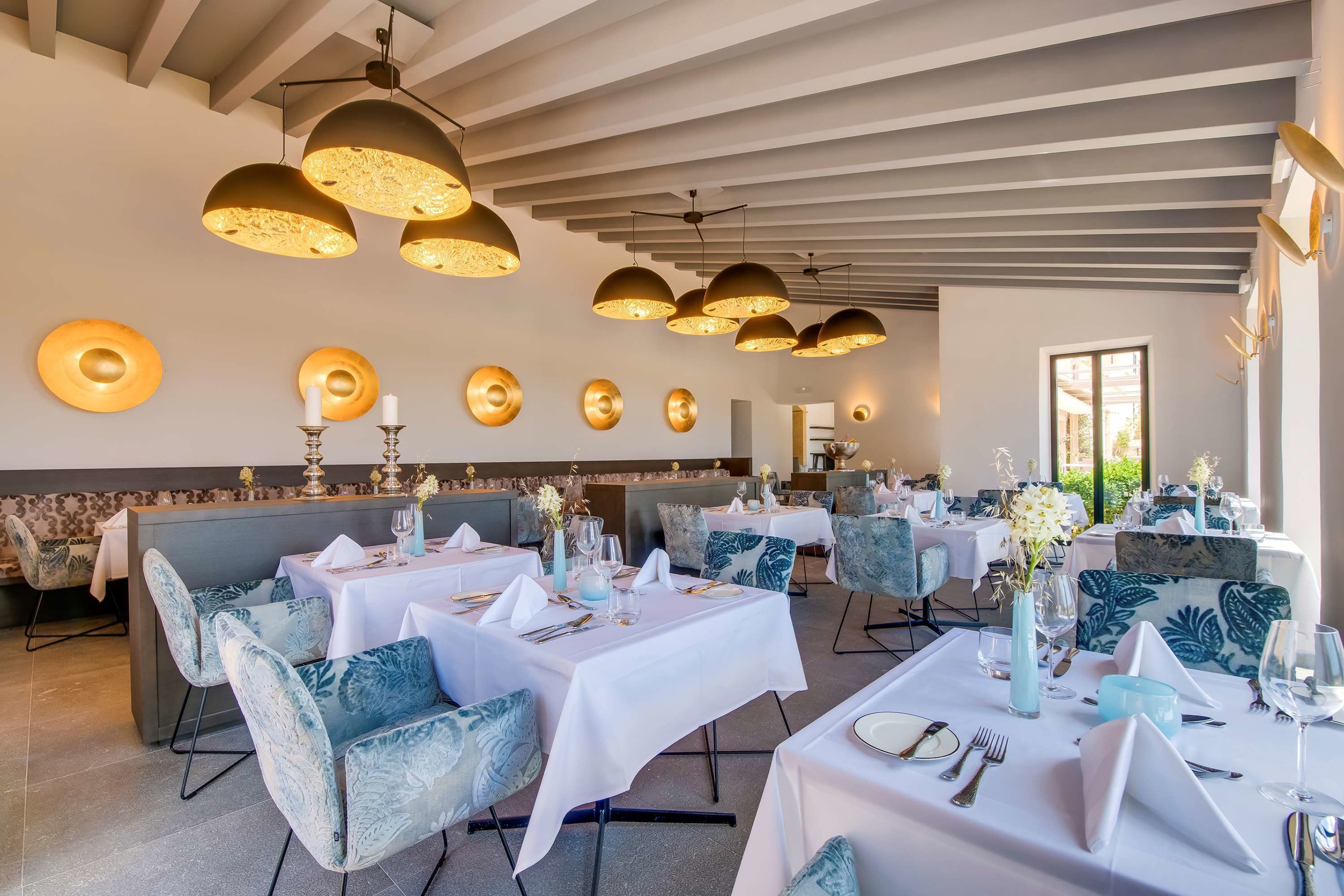 A restaurant with white tablecloths, blue upholstered chairs, and gold pendant lighting.