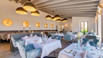 A restaurant with white tablecloths, blue upholstered chairs, and gold pendant lighting.