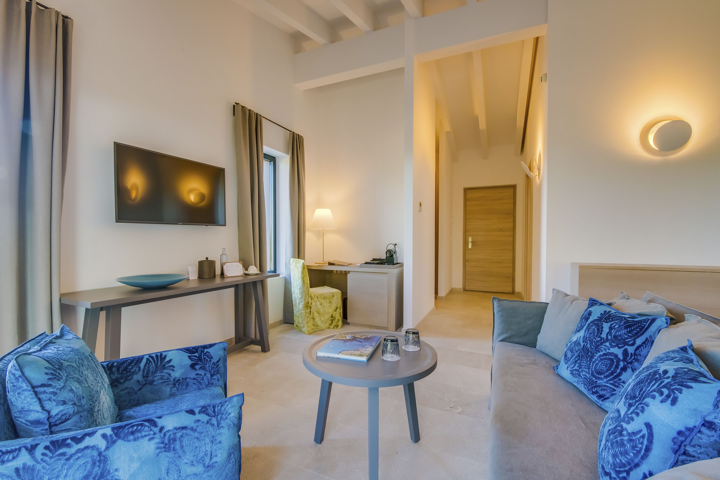 Una sala de estar moderna con un sofá, sillones, una mesa de centro, un televisor y un escritorio con una lámpara.