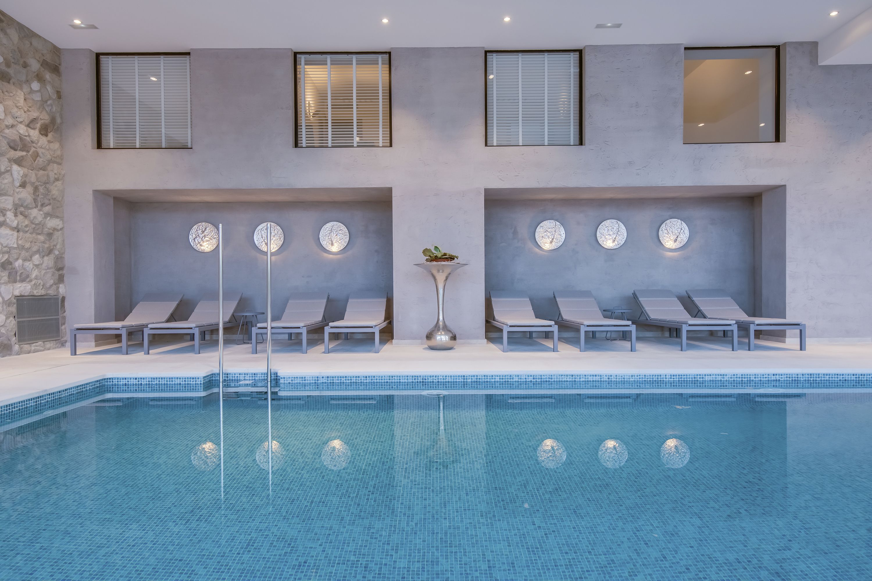 Una piscina interior moderna con sillones de descanso e iluminación empotrada.