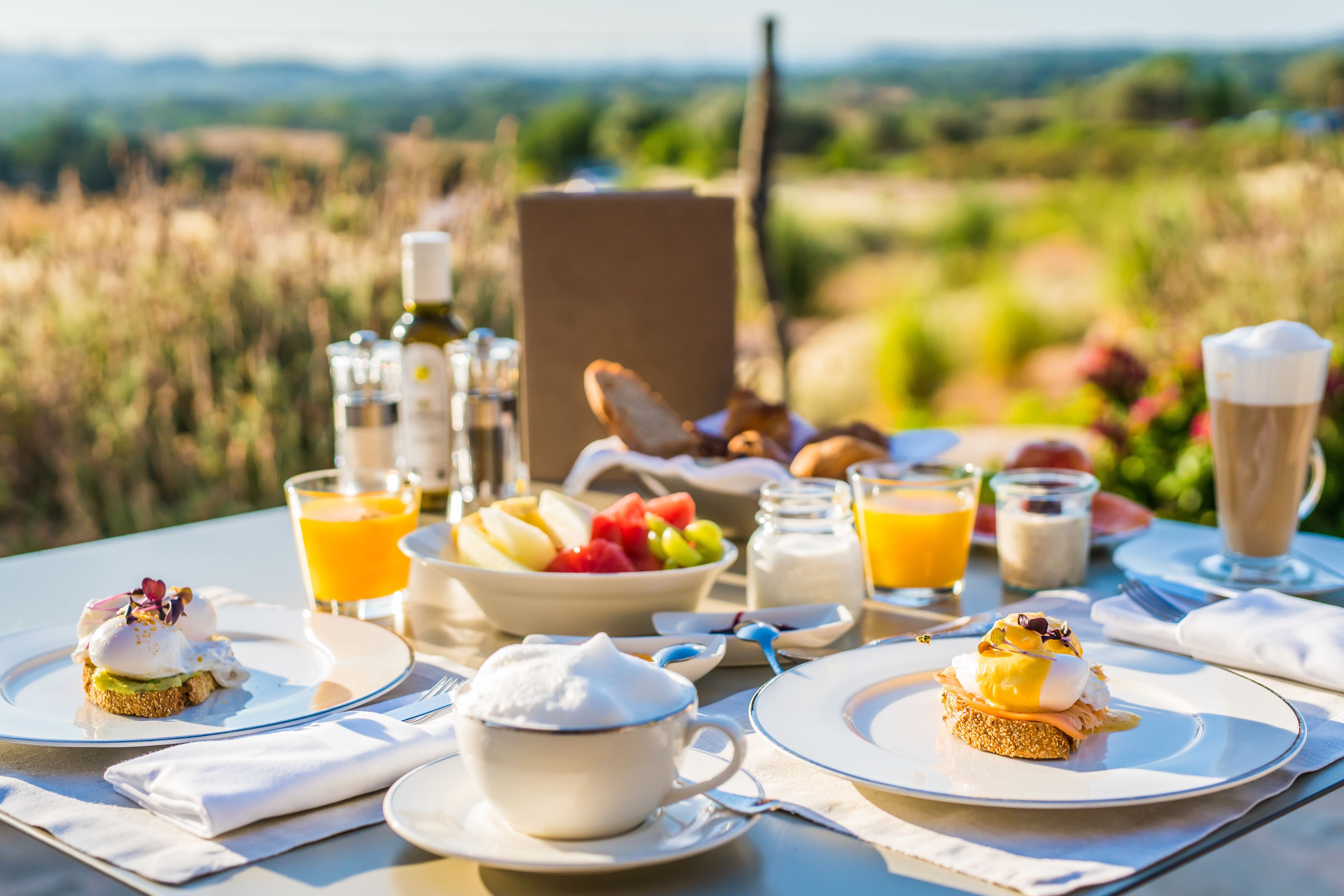 Desayuno con diversos platos, entre ellos huevos, tostadas y fruta, sobre una mesa con una vista panorámica de fondo.