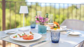 Una mesa dispuesta con un plato de comida, una copa de vino y un jarrón de flores en una terraza al aire libre.