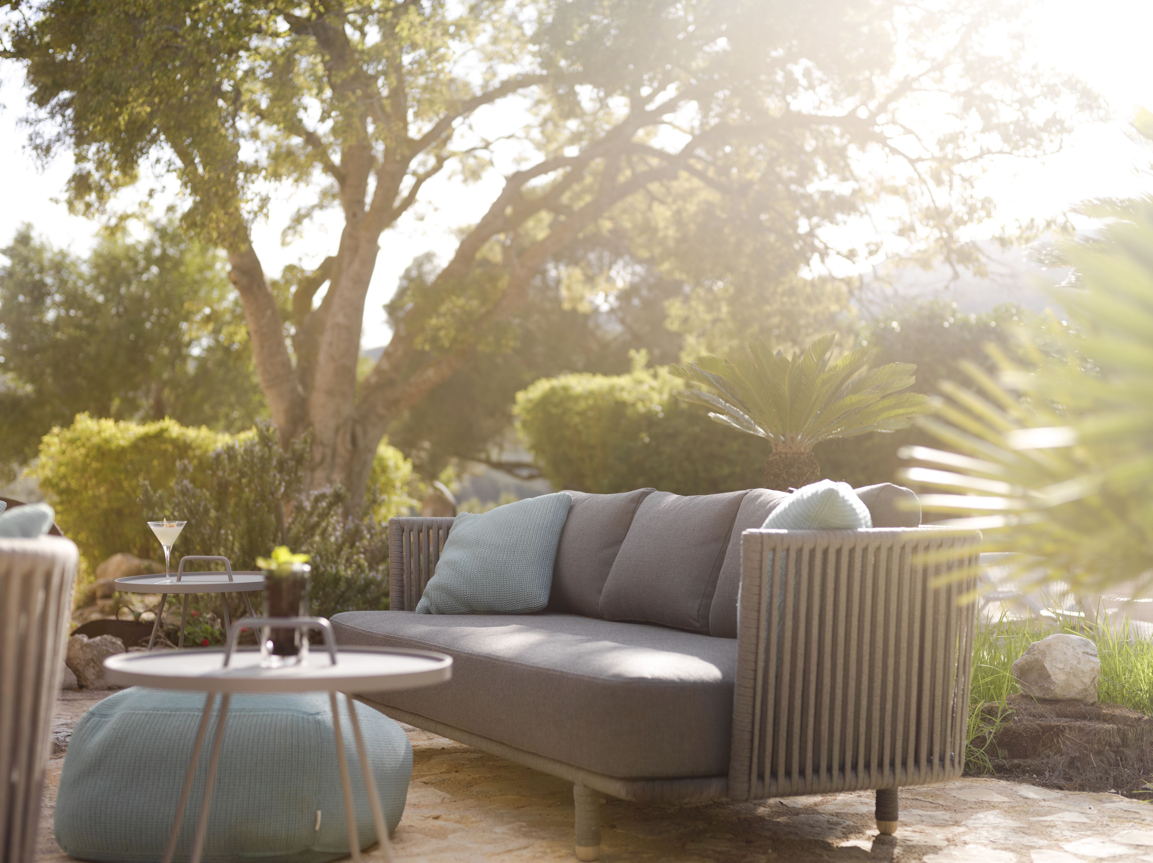 An outdoor seating area with a sofa, round table, and chairs, surrounded by greenery and trees.