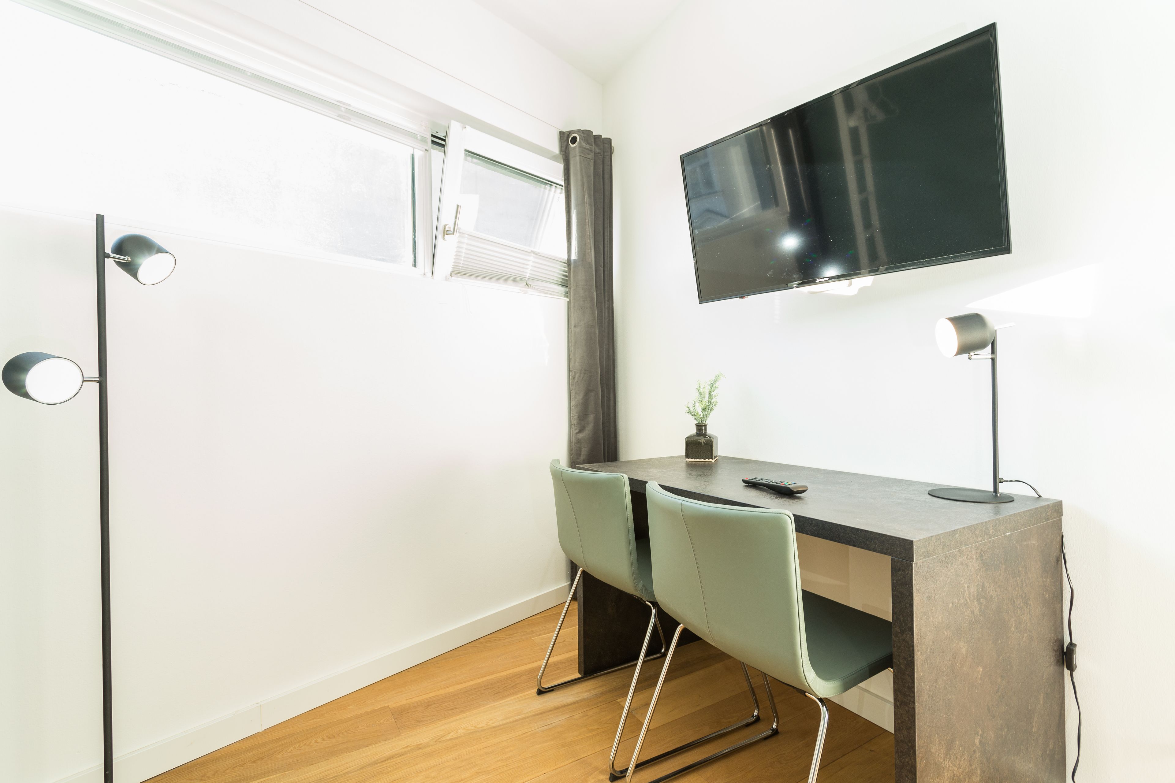 Ett modernt rum med ett skrivbord, två stolar, en tv och ett fönster med gardiner.
