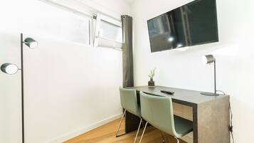 Ett modernt rum med ett skrivbord, två stolar, en tv och ett fönster med gardiner.