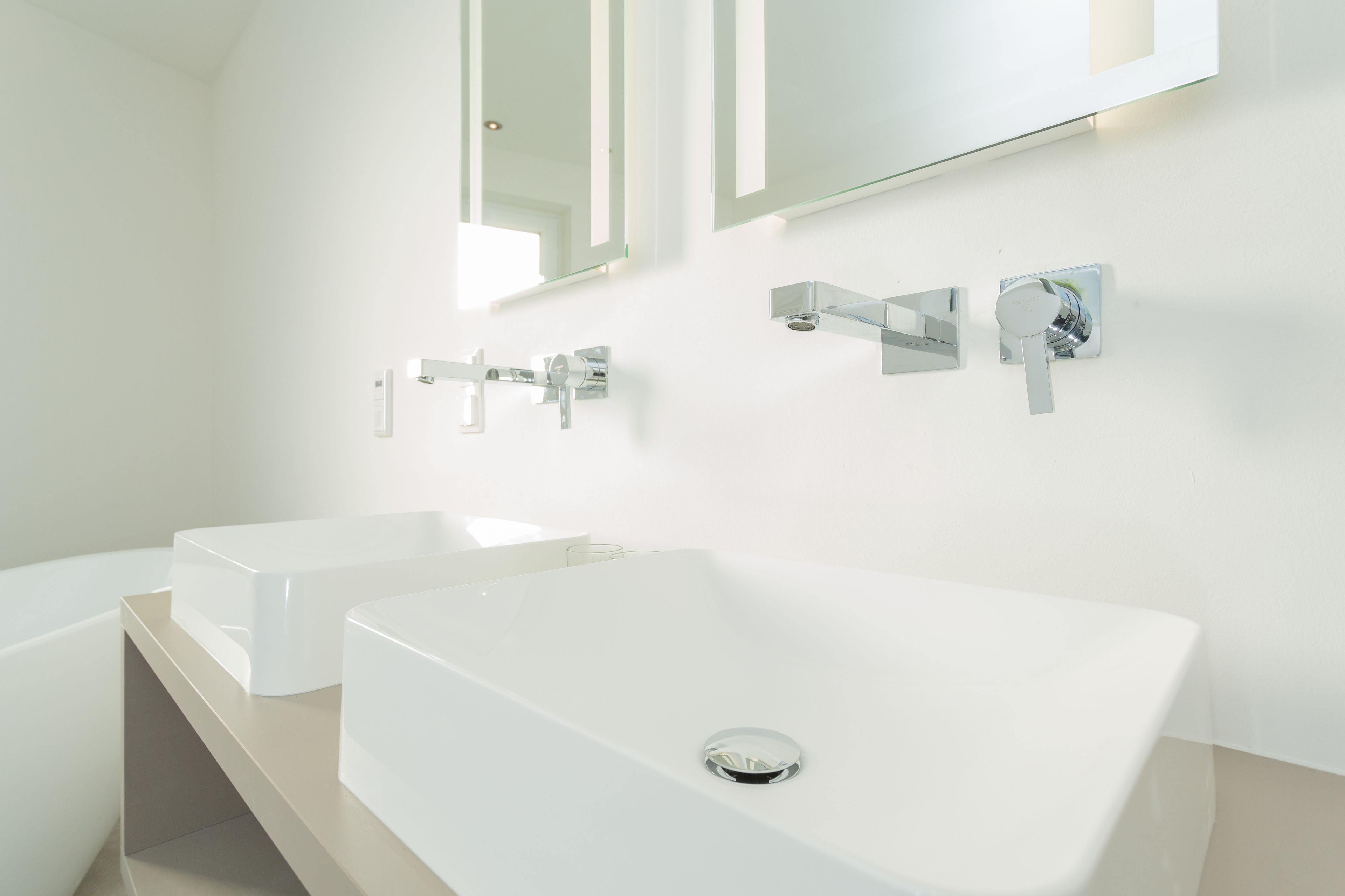 A modern bathroom with two white sinks, chrome faucets, and a large mirror above.