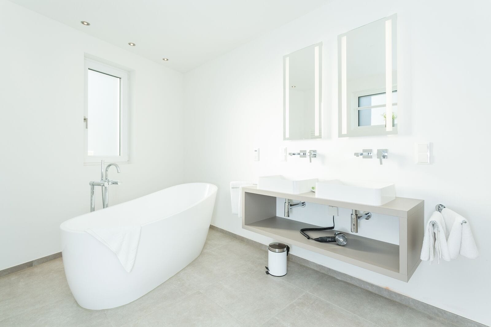 Ein modernes Badezimmer mit einer freistehenden Badewanne, einem Waschtisch mit Spüle und zwei Spiegeln darüber.