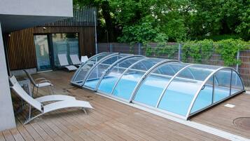 Una piscina techada con sillas de descanso y una terraza de madera.