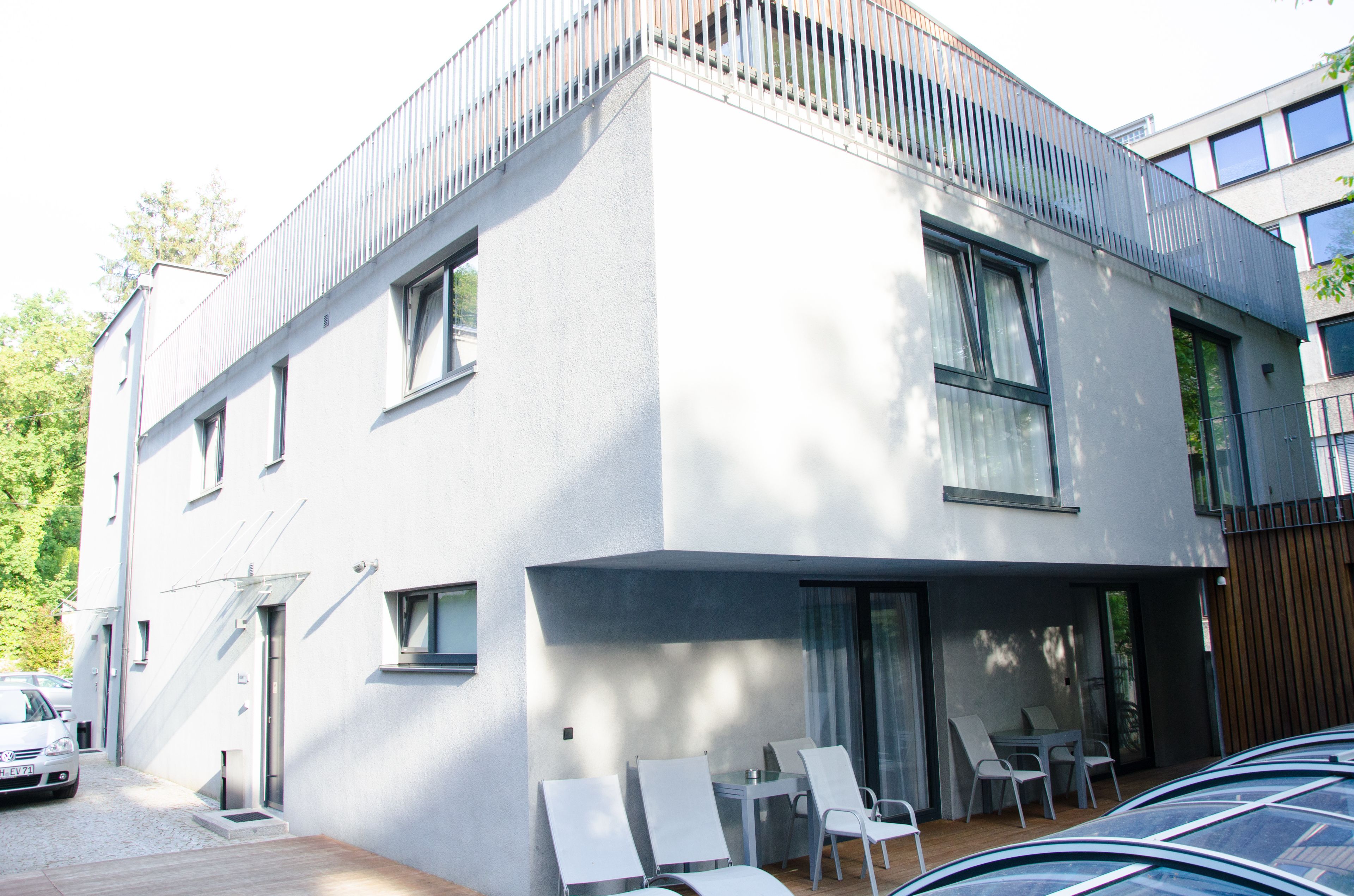 Un bâtiment moderne à deux étages, doté d’un toit plat, de grandes fenêtres et d’un balcon avec des chaises.