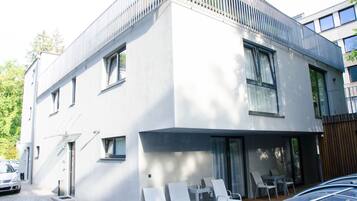 Un bâtiment moderne à deux étages, doté d’un toit plat, de grandes fenêtres et d’un balcon avec des chaises.