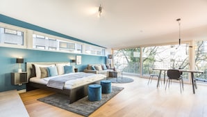 A modern bedroom with a large bed, bedside tables, a desk, and a view of the outdoors. - Room 4 & 5 Apartments (Salzburg)