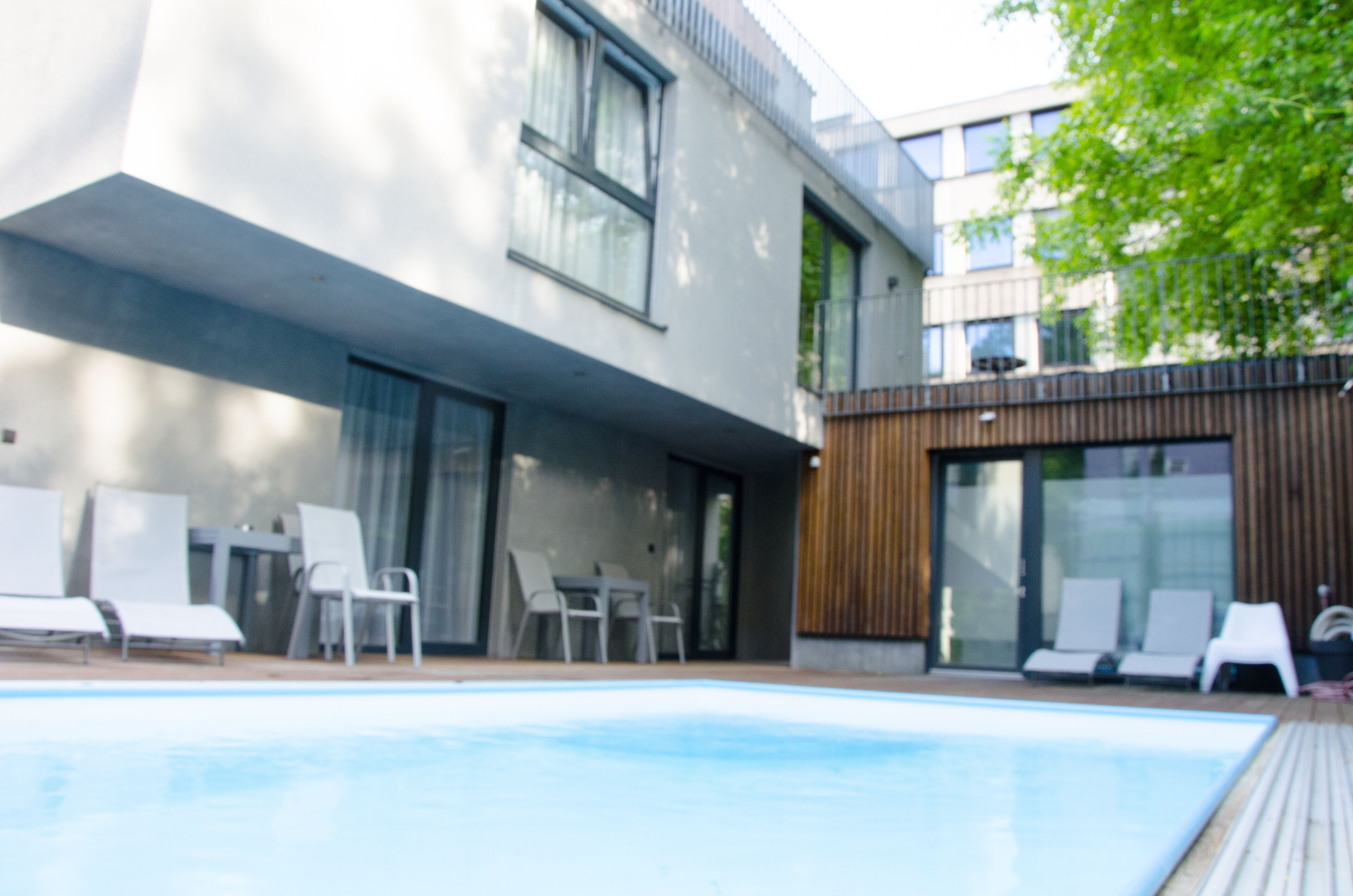 Een modern gebouw met een zwembad, ligstoelen en een houten terras.