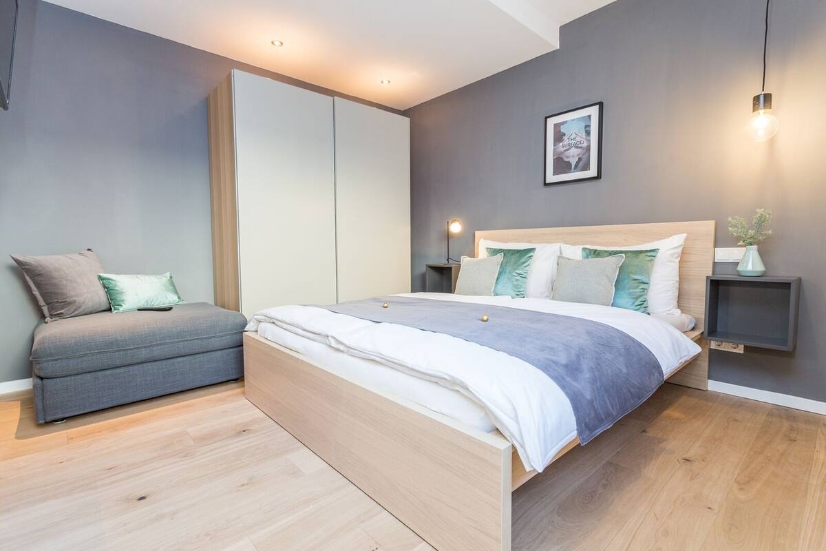 Quarto moderno com cama, mesas de cabeceira, sofá e guarda-roupa.