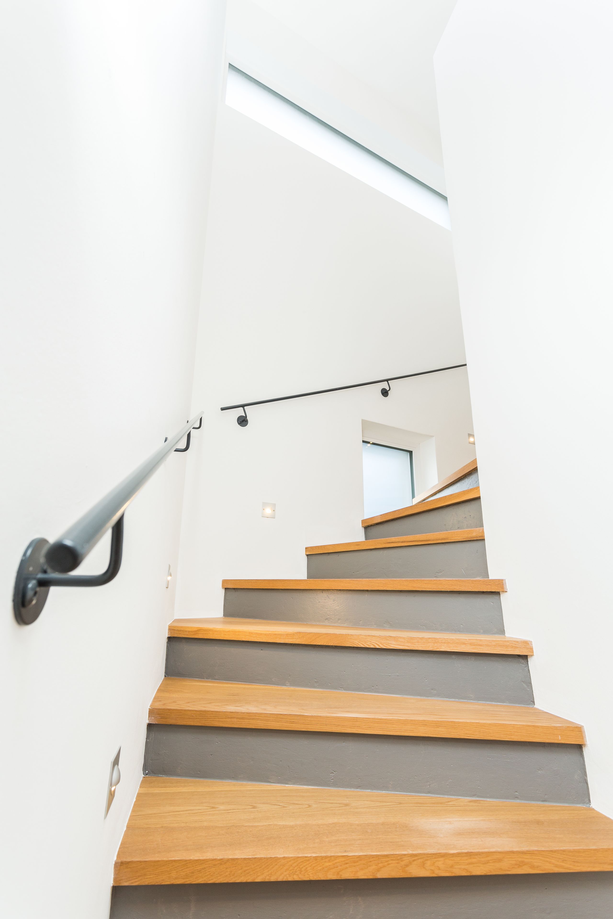 Un escalier moderne avec des marches en bois et une rampe en métal, menant à l’étage supérieur.