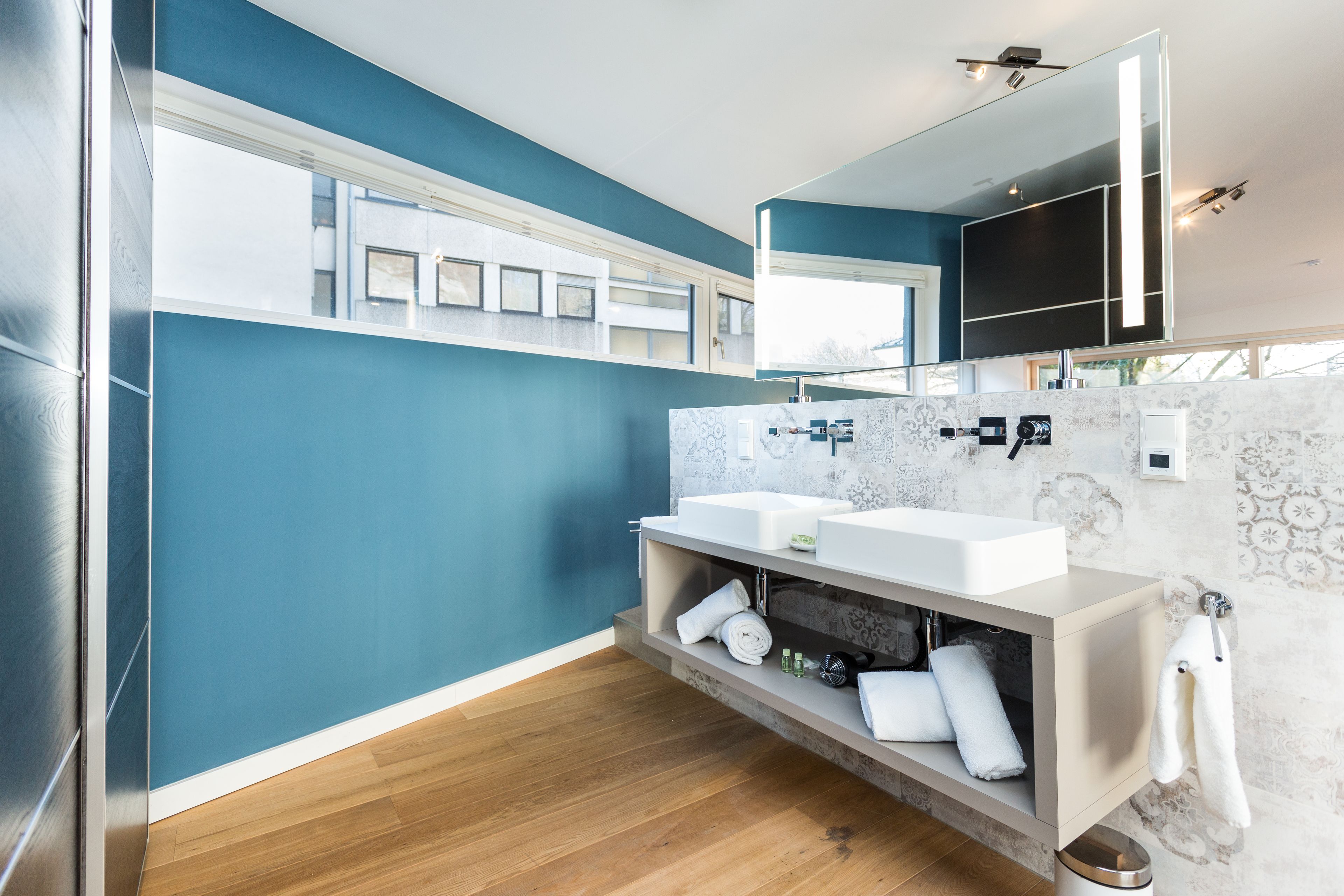 A modern bathroom with two sinks, a large mirror, and a built-in shelf with towels.