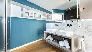 A modern bathroom with two sinks, a large mirror, and a built-in shelf with towels.