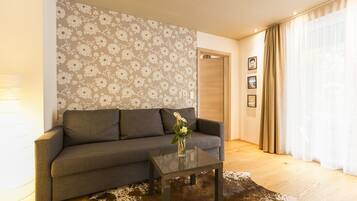 A living room with a sofa, a coffee table, a floral wallpaper, and a wooden floor.