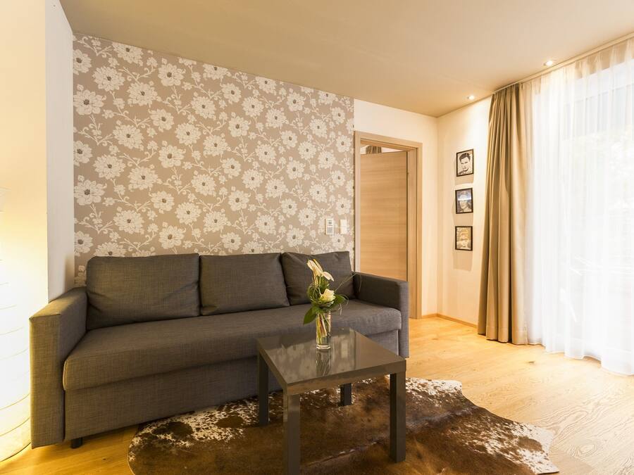 Un salón con sofá, mesa de centro, papel tapiz floral y suelo de madera.