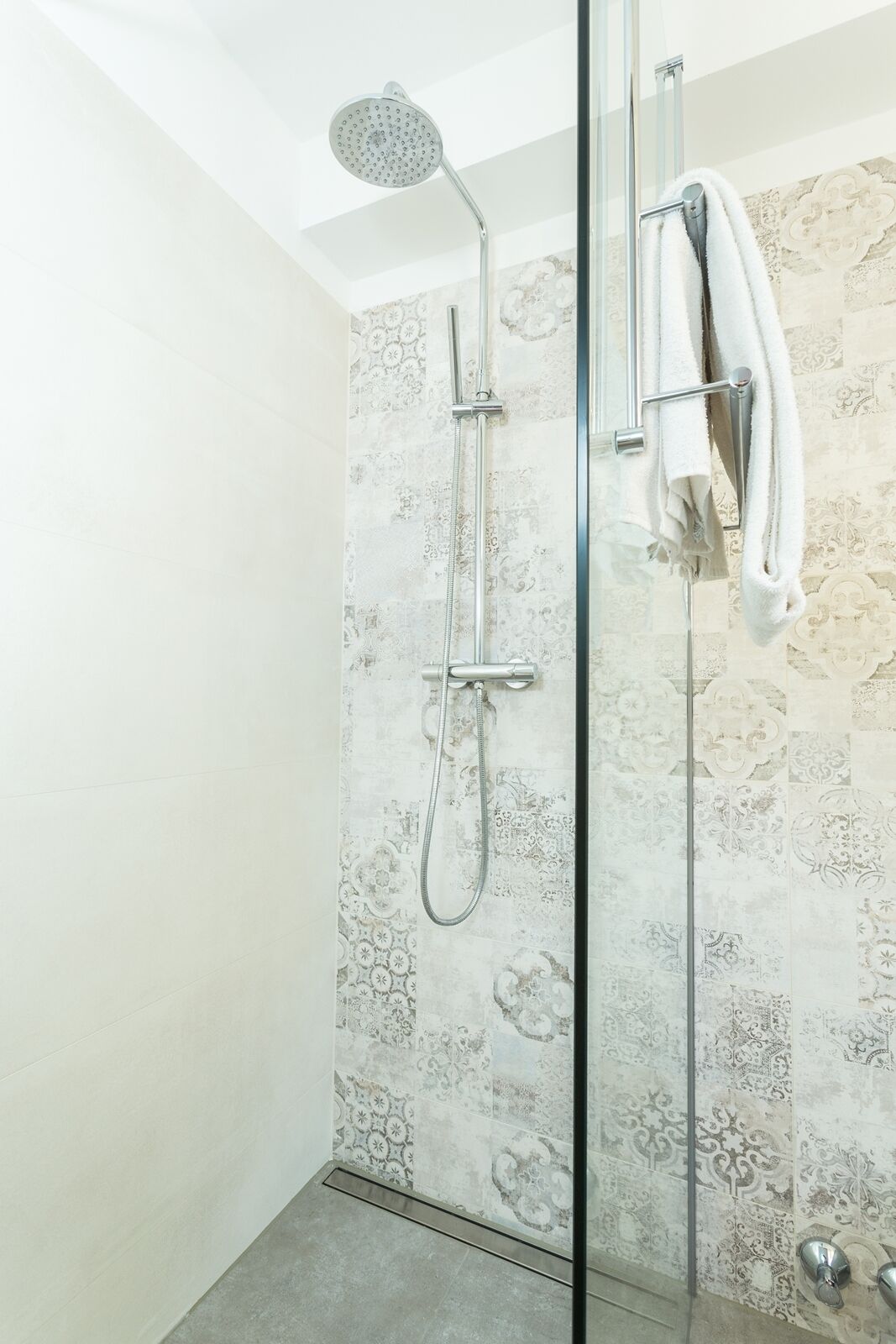 A glass-enclosed shower with a handheld showerhead and a wall-mounted faucet.