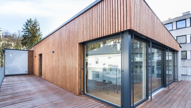 A modern building with a wooden exterior, large glass windows, and a wooden deck. - Room 4 & 5 Apartments (Salzburg)